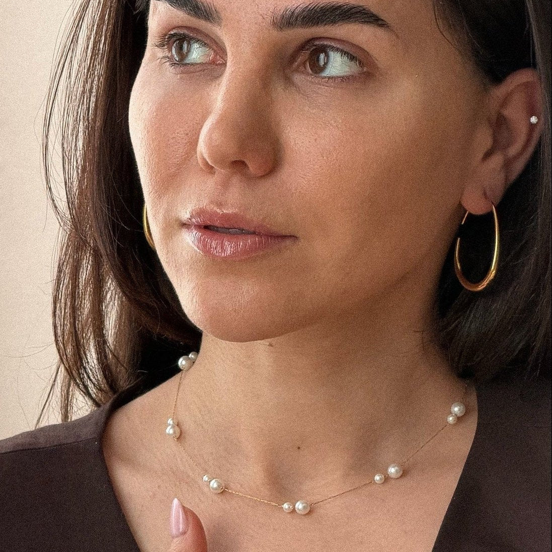 Dark-haired woman wearing the gold hoop with a fine pearl necklace
