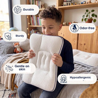 Boy sitting on a bed holding the pillow, with labels for durable, sturdy, odor-free, gentle on skin and hypoallergenic.