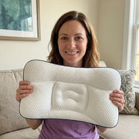 Smiling woman on a sofa holding the pillow up towards the camera with both hands.