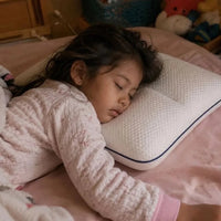 Young girl asleep on her side with her head resting on the pillow in a softly lit bedroom.