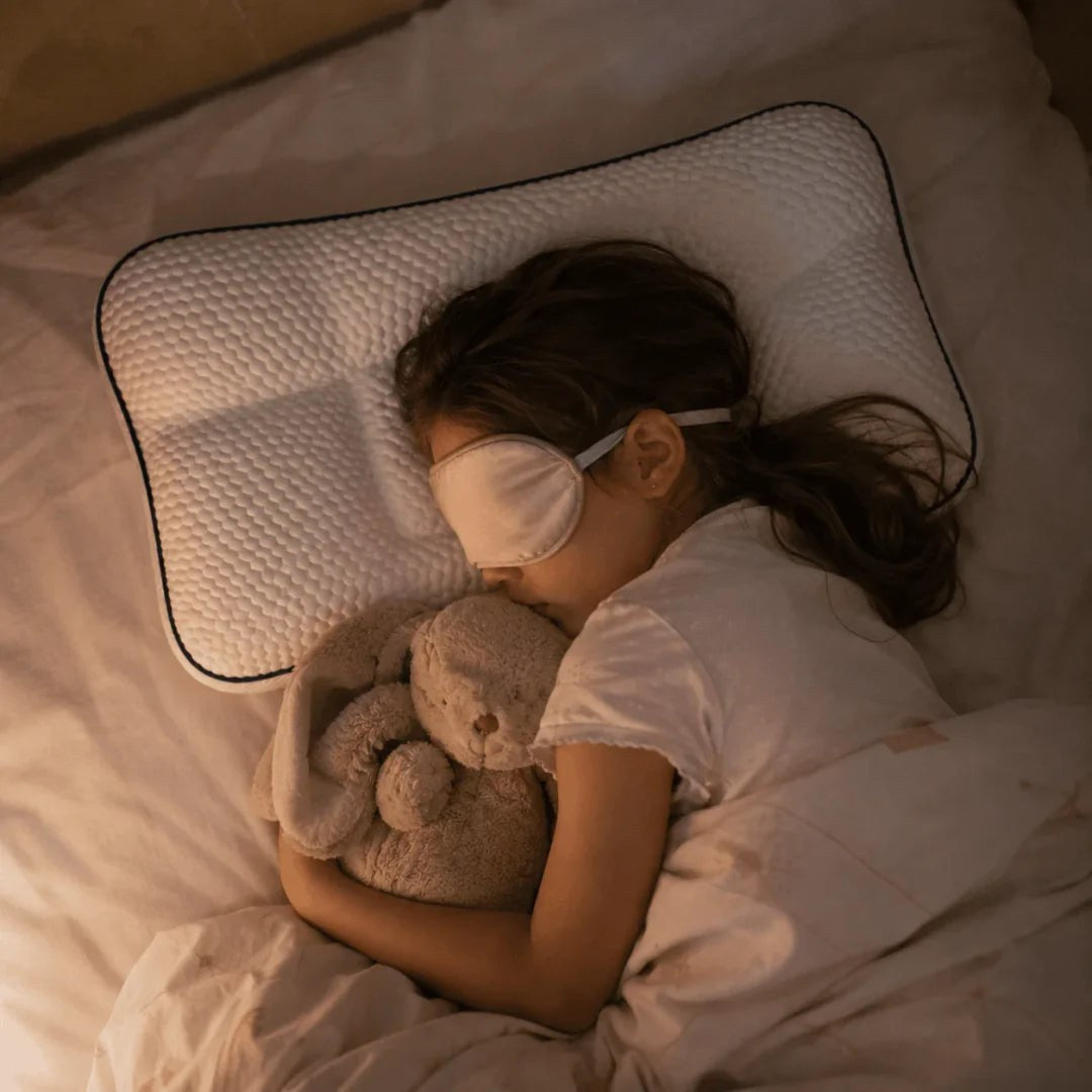 Girl asleep on the pillow at night wearing a sleep mask and holding a plush bunny, seen from above.